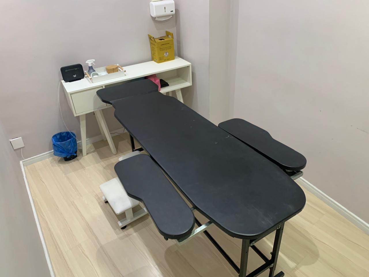 Sala de atendimento com maca preta e mesa auxiliar